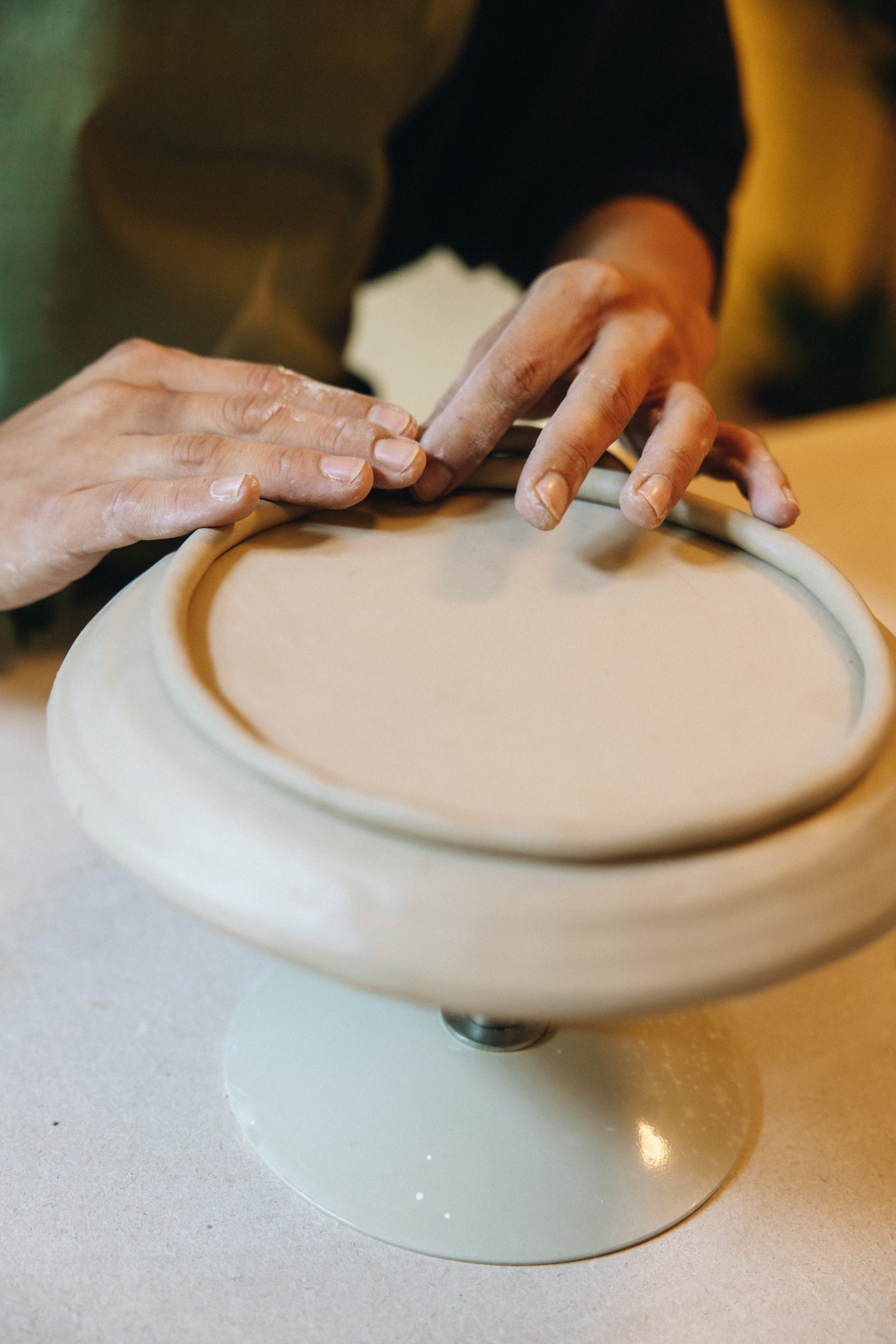 Handaufbau im Töpferkurs Wien - Hände formen einen Fußring auf Platte aus Ton in Verenics Töpferstudio.